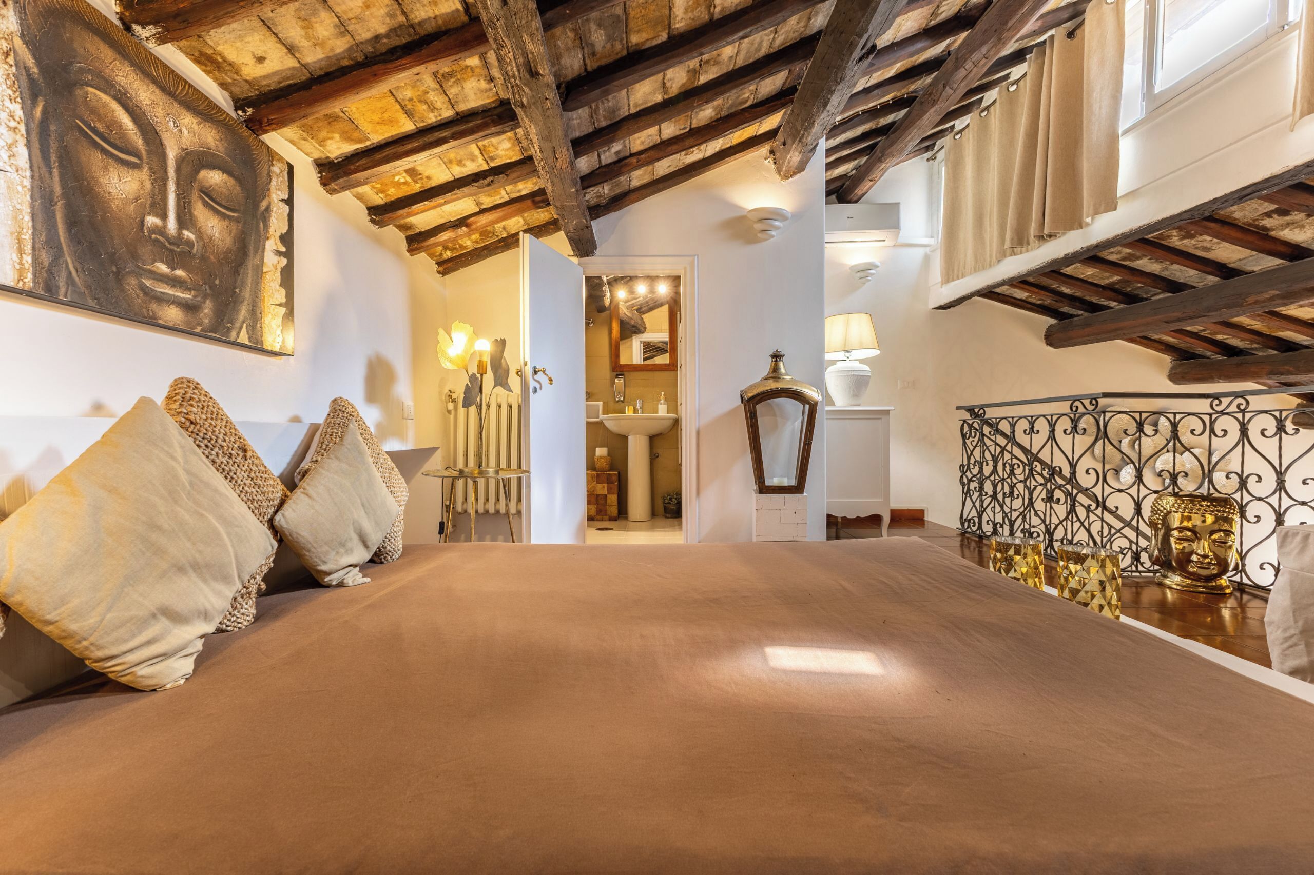 A room with a bed, a wooden ceiling, a Buddha statue, and a window.