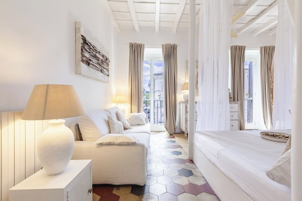 A room with a bed, a sofa, a lamp, and a view of the outside.