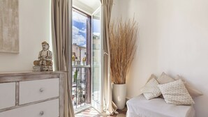 Un dormitorio con cama, cómoda, ventana con cortinas y vista a edificios.