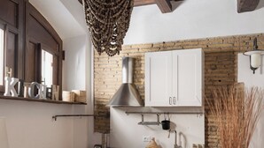 Une cuisine avec un plafond en bois rustique, des armoires blanches, un luminaire suspendu et un sol carrelé.
