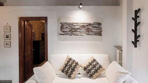 Un canapé blanc avec des coussins à motifs, un élément décoratif mural de style rustique, une porte en bois et un porte-manteau noir.