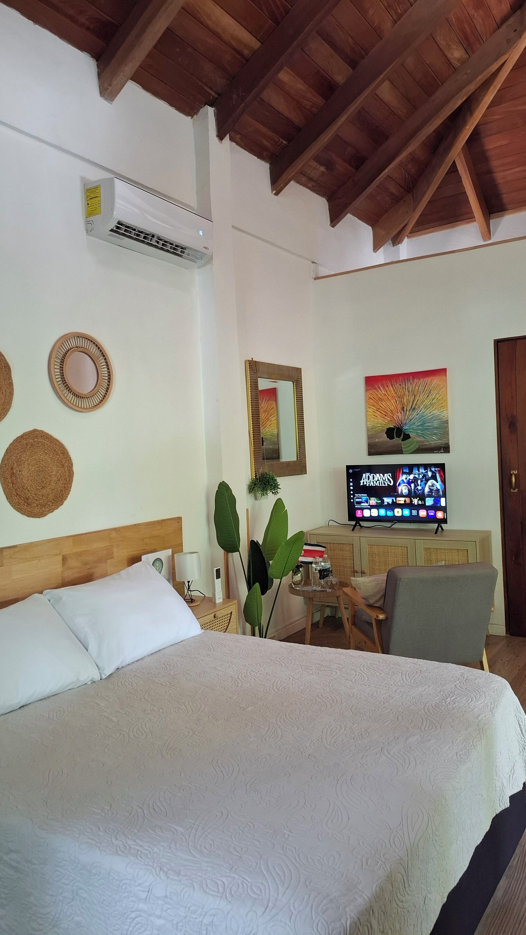 Um quarto com cama, televisão, escrivaninha e espelho.