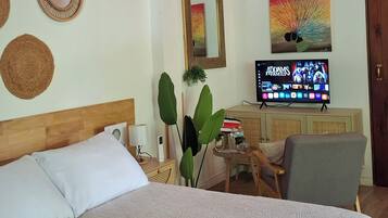 Um quarto com cama, televisão, escrivaninha e espelho.