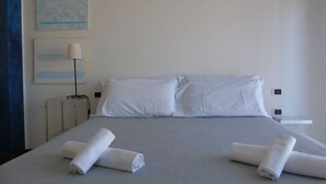 A neatly made bed with white linens and rolled towels, a bedside table with a lamp, and a wall-mounted artwork. - Homiday - Residence Prestige, Interno 10 (Pineto)