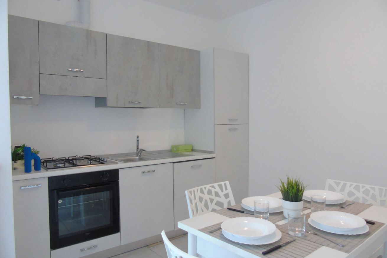 A modern kitchen with white cabinets, a built-in oven, and a dining area with a table set for four.