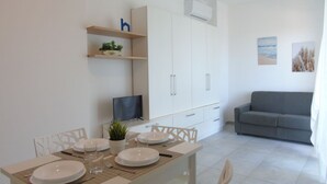 Una zona de menjador amb una taula preparada per a quatre persones, una televisió i un sofà gris al fons.