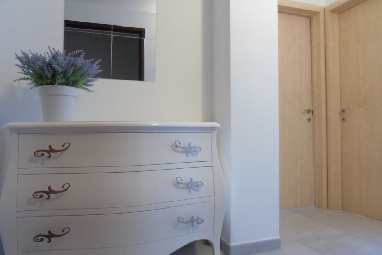 Une commode blanche avec des poignées décoratives, une plante en pot et un miroir au-dessus.
