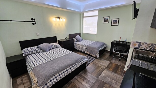 Une chambre avec deux lits, un bureau, une chaise et une petite kitchenette.