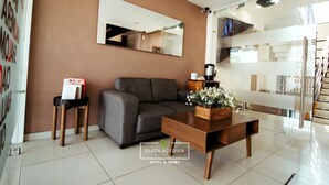 A modern living room with a sofa, coffee table, and a mirror on the wall. There is a sign for 'Plaza Acequia Suites & Rooms'.