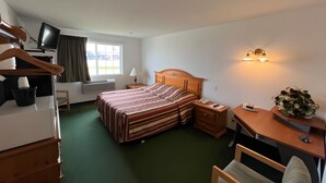 Una habitación de hotel con cama, escritorio, silla, televisión y ventana con cortinas.