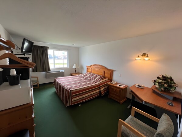 A hotel room with a bed, a desk, a chair, a TV, and a window with curtains.