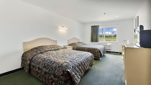Habitación de hotel con dos camas, un escritorio, un televisor y ventana con vistas al exterior.