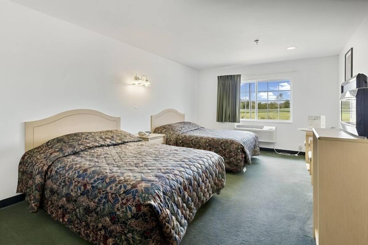 A hotel room with two beds, a desk, a television, and a window with a view of the outdoors.