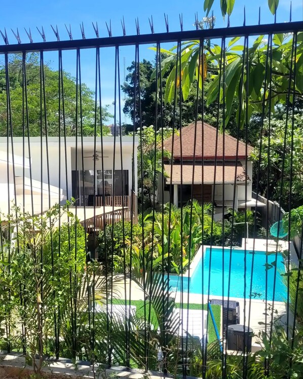A residential area with a swimming pool, surrounded by lush greenery and a metal fence.
