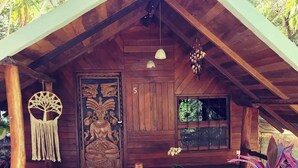 A wooden cabin with a sloped roof, a large carved door, and a small porch area with plants. - sharonus cabin (Tamarindo)