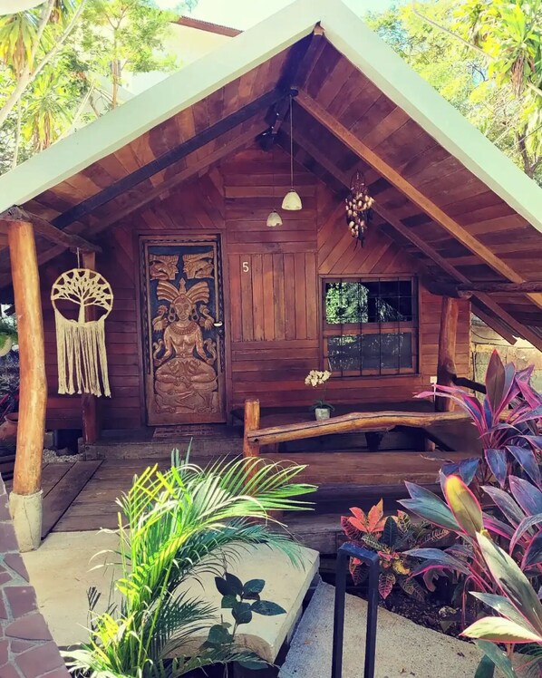 Una cabaña de madera con techo inclinado, una puerta grande tallada y un pequeño porche con plantas.