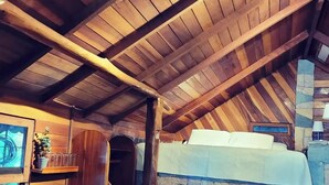 A rustic wooden interior with a sloped ceiling, a stone fireplace, and a bench. - sharonus cabin (Tamarindo)