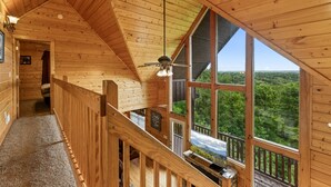 Ein Holzblockbau-Innenraum mit hohen Decken, einer Treppe zu einem Balkon und großen Fenstern mit Blick auf den Wald.