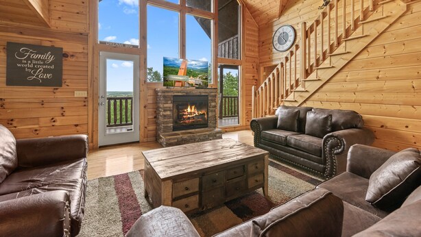 Ein gemütliches Blockhaus-Interieur mit Kamin, Ledersofas, einem Holztisch und einer Treppe.