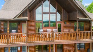 Eine Blockhütte mit Balkon und großen Fenstern, die einen Blick auf die umliegende Landschaft freigeben.