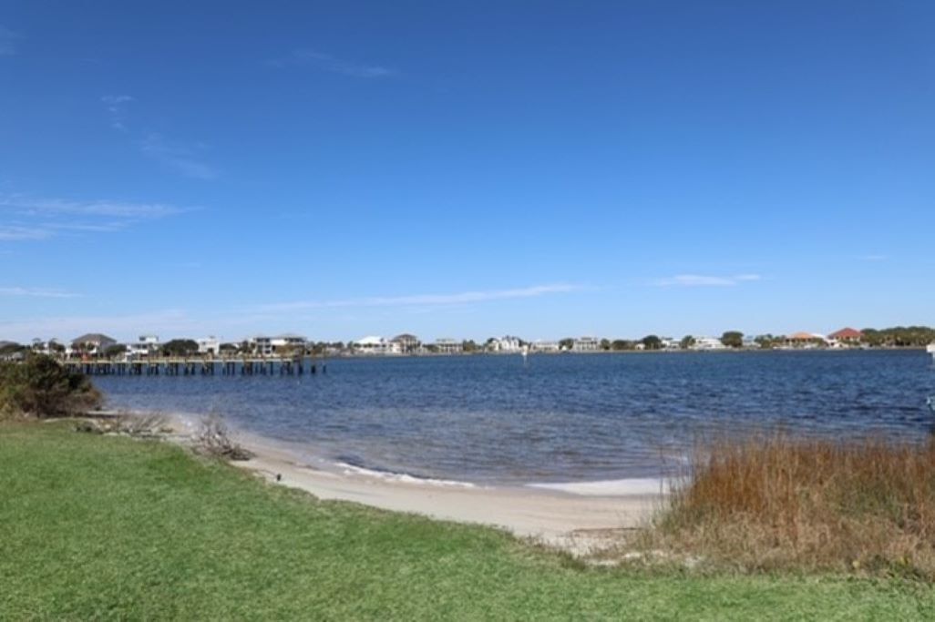 A beach with a clear view of the water and a distant shoreline with buildings.