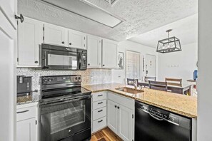 A compact kitchen with white cabinets, a built-in microwave, a stove, and a dishwasher.