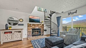 A modern living room with a fireplace, a staircase, and a view of the outdoors. - Mountain View Condo w/ Indoor Pool & Hot Tub (Gatlinburg)