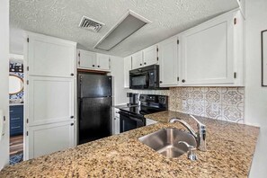 Cocina con armarios blancos, encimera de granito, pileta de acero inoxidable, electrodomésticos negros y salpicadero con diseño.