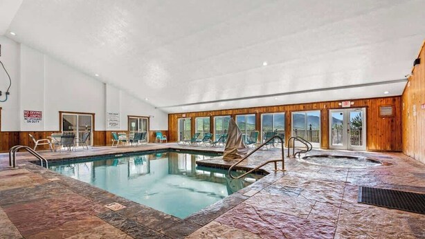 An indoor swimming pool with a stone floor, lounge chairs, and a view of the outdoors through large windows. - Mountain View Condo w/ Indoor Pool & Hot Tub (Gatlinburg)