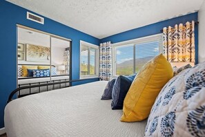 A bedroom with a large bed, a mirror, and a window with curtains.