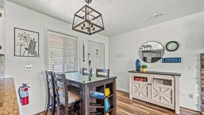 A dining area with a glass-top table, wooden chairs, a pendant light, a white cabinet with a mirror, and a clock on the wall. - Mountain View Condo w/ Indoor Pool & Hot Tub (Gatlinburg)