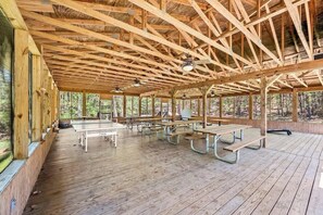 A covered picnic area with wooden benches and picnic tables, surrounded by large windows.