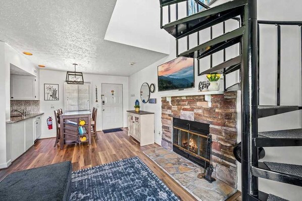 A modern living room with a fireplace, a dining area, and a staircase.
