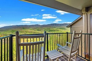 A balcony with two wooden chairs and a table, overlooking a mountainous landscape.