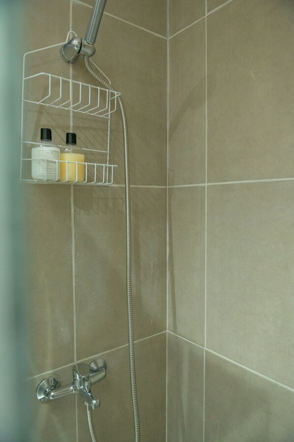 A shower area with a chrome showerhead, a handheld shower attachment, and a wall-mounted shelf with toiletries.