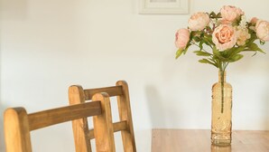 Una mesa de madera para comer con un jarrón de flores rosas y dos cuadros en la pared.