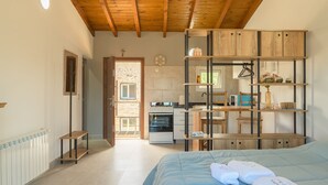 Un dormitorio con cama, cabecera de madera, repisa con toallas y vista a una cocina y un baño a través de una puerta abierta.