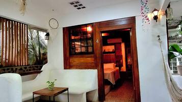 Una habitación con un sofá blanco, una mesita, una planta colgante y un acceso a otra estancia.