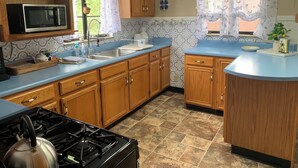 A kitchen with wooden cabinets, a microwave, a sink, and a stove. - The Kitchie Kottage/ House (Portsmouth)