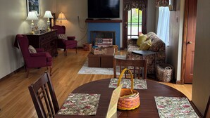 A dining area with a round wooden table, floral placemats, and a ceiling fan with light fixtures. - The Kitchie Kottage/ House (Portsmouth)