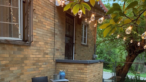 An outdoor patio area with wicker furniture, a brick wall, and string lights. - The Kitchie Kottage/ House (Portsmouth)