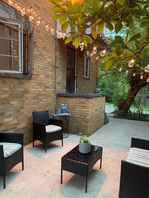 An outdoor patio area with wicker furniture, a brick wall, and string lights.