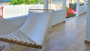 A hammock on a wooden deck with a view of palm trees and a house in the background. - Casa Colorá - Private Pool - Near Beach & Restaurants - 3BR - Close to El Yunque (Naguabo)