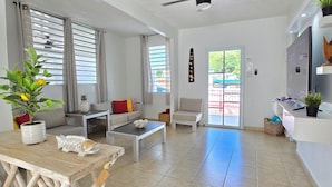 A spacious living room with a ceiling fan, a sofa, a coffee table, and a dining area with a wooden table and chairs. - Casa Colorá - Private Pool - Near Beach & Restaurants - 3BR - Close to El Yunque (Naguabo)