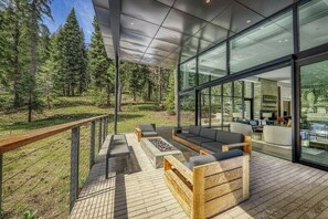 A modern outdoor deck with seating, a fire pit, and a view of a forest.
