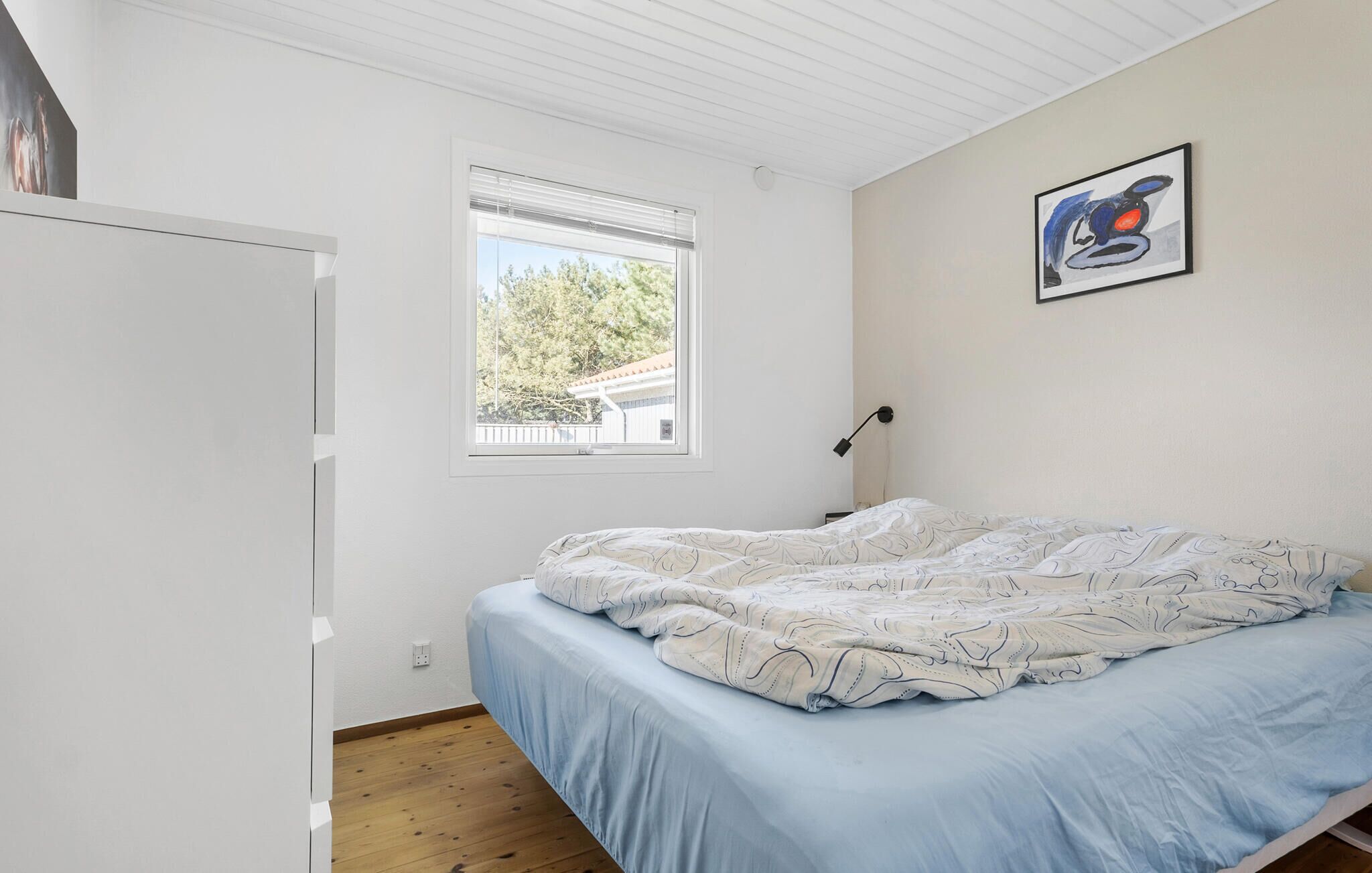 A bedroom with a bed, a window, and a wall-mounted lamp.