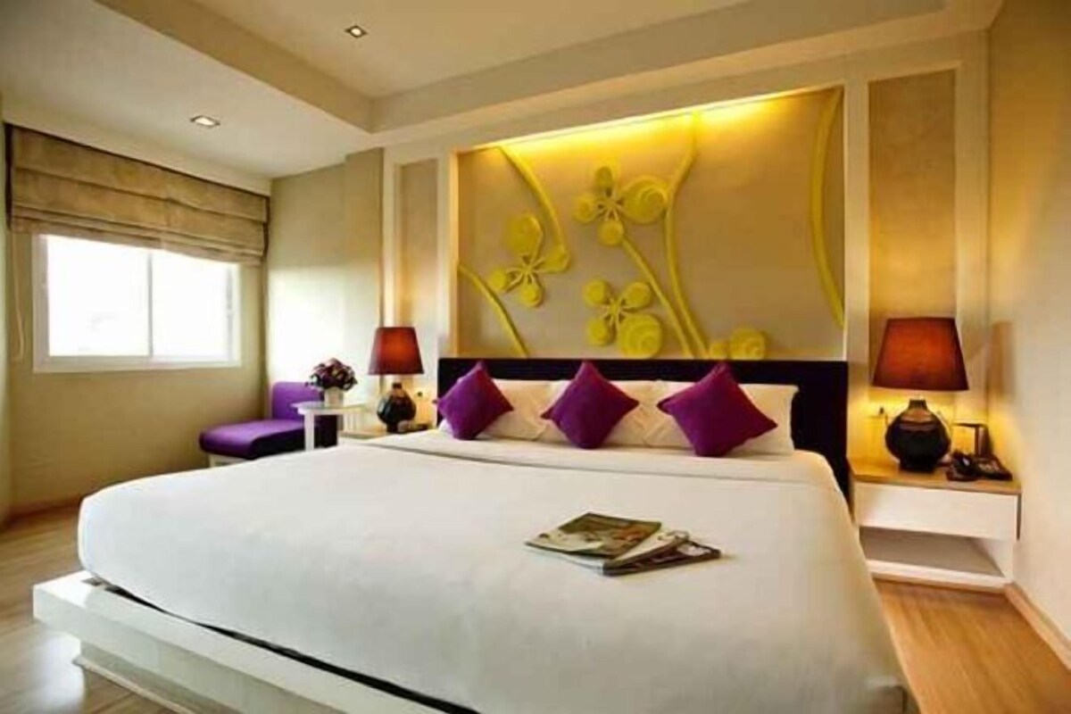 Une chambre d’hôtel avec un grand lit, une table de chevet, une chaise et un mur orné d’un motif floral.