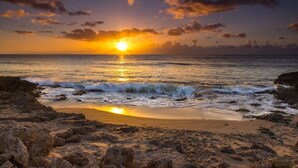 Ein Strand mit Sonnenuntergang, felsigem Ufer und ruhiger See.