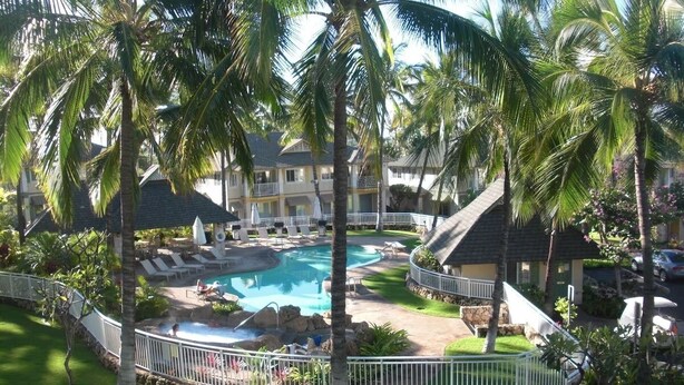 Ein Resort mit zentralem Schwimmbecken, Liegestühlen und Palmen.