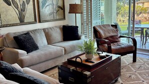 Ein Wohnzimmer mit einer Couch, einem Sessel und einem Couchtisch mit Pflanze und Fernbedienung.